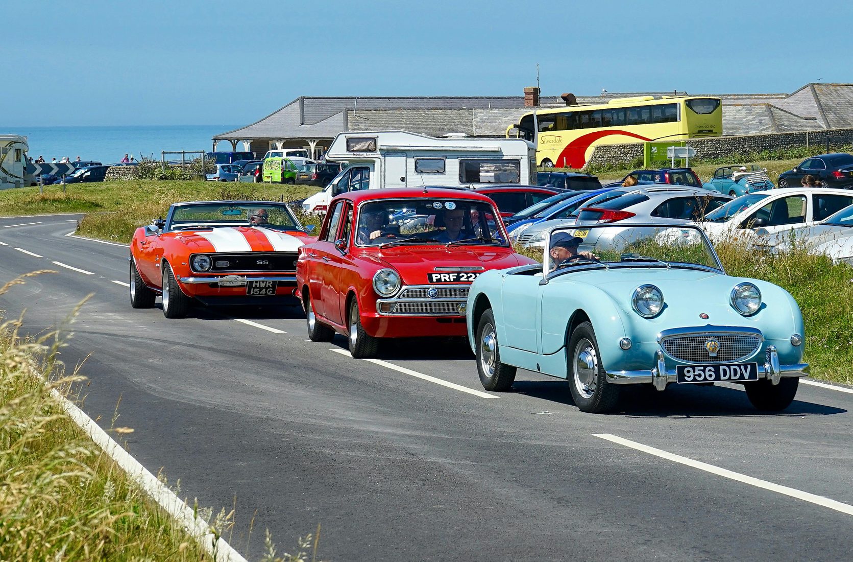 A line of classic cars driving together on a coastal road